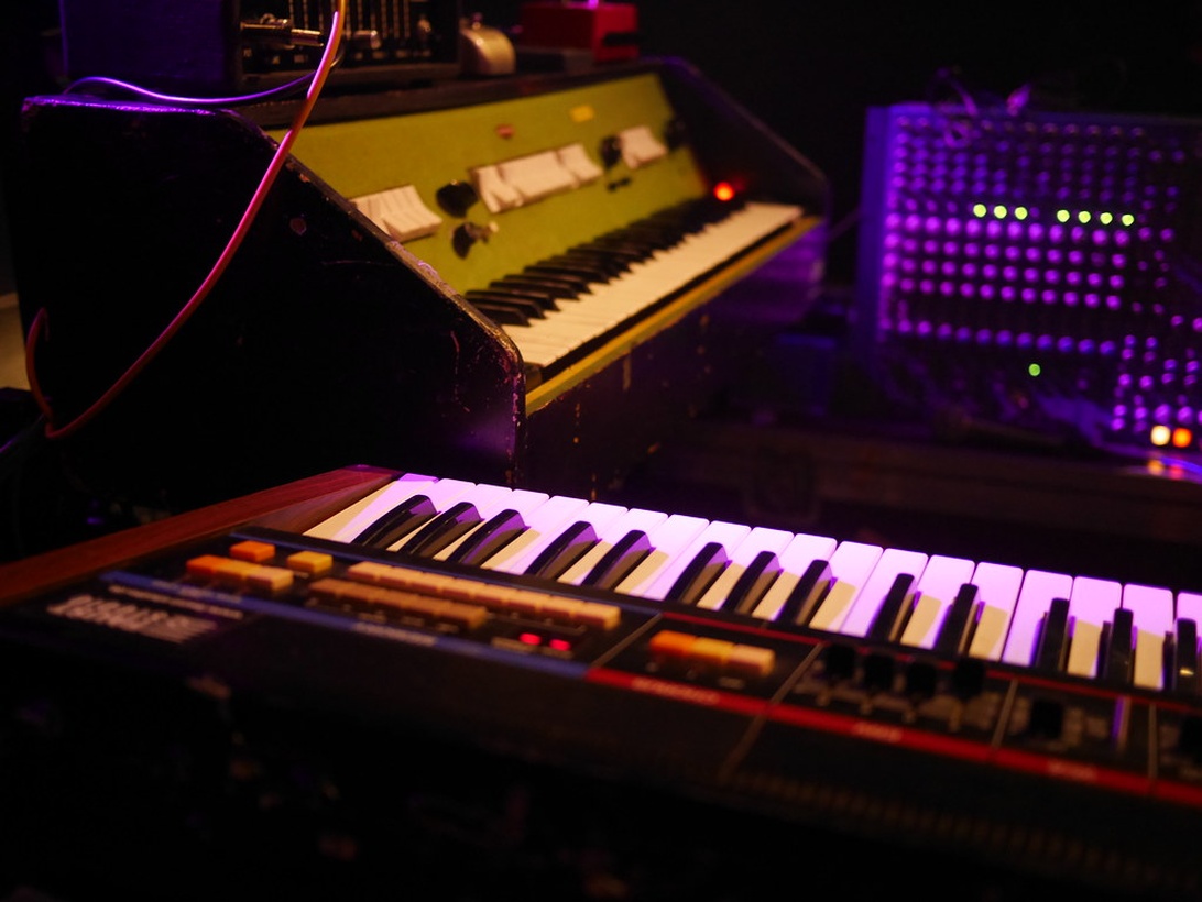 A music production studio with vintage synthesizers and modern keyboards illuminated by colorful LED lights.